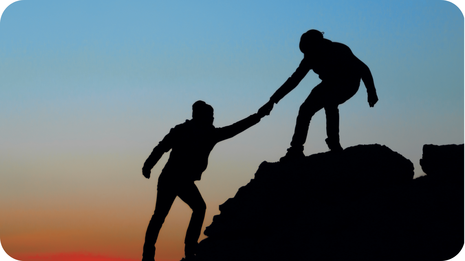Silhouette of one hiker reaching down to help another climb a ridge at sunset